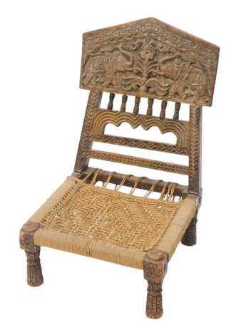 Tribal Art. An Indian pidha tribal chair, the hinged back carved with elephants, flowers, etc., with a woven seat, on tapering legs, 49cm wide.