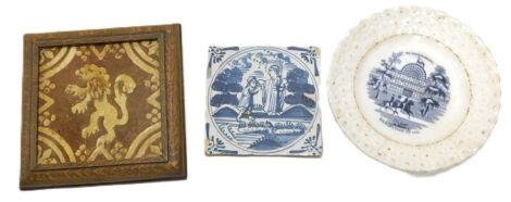 A 17thC Delft tile in blue, with a Saint bestowing a blessing, 13cm wide, a commemorative plate, and a tile decorated with a lion. (3)