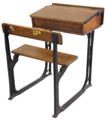 A 20thC oak school desk, with ink recess, a sloping hinged lid enclosing a vacant interior, with integrated bench, on a cast iron support, 81cm high.