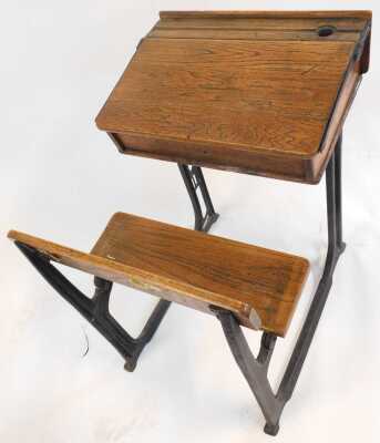 A 20thC oak school desk, with ink recess, a sloping hinged lid enclosing a vacant interior, with integrated bench, on a cast iron support, 81cm high. - 2