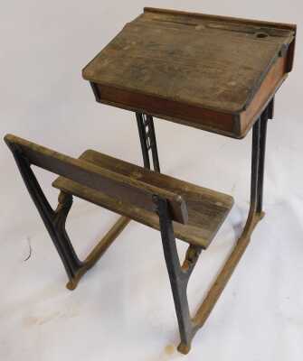 A 20thC oak school desk, with ink recess, a sloping hinged lid enclosing a vacant interior, with integrated bench, on a cast iron support, 81cm high. (AF) - 2