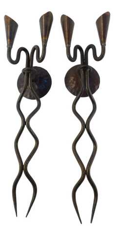 A pair of 20thC wrought iron twin wall mounted candle holders, the wall bracket of circular form with trumpet shaped candle holders, supported by a waved long stem, 60cm high.