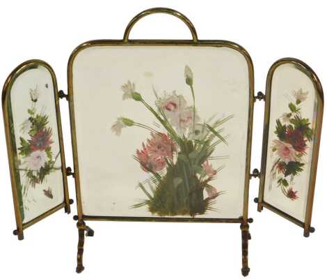 An early 20thC brass framed three fold fire guard, each mirrored panel decorated with flowers, 64cm high.