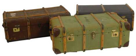 Three early 20thC travelling trunks, each wooden bound, two in canvas brown and green and the other in brown leather, bearing labels, each 83cm wide.