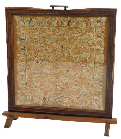 An early 20thC oak framed fire screen, inset with an embroidered panel decorated with leaves, scrolls, etc., 80cm high, 76cm wide, 22cm deep.