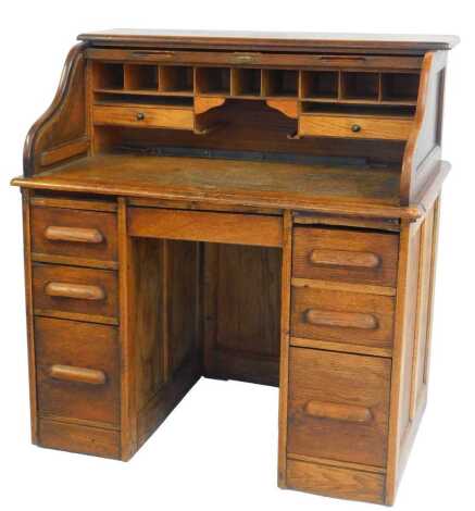 A 1920s oak roll top desk, the tambour front enclosing an arrangement of drawers, above three graduated drawers to each pedestal, on a block base on castors, with key, 117cm high, 106cm wide, 65cm deep.