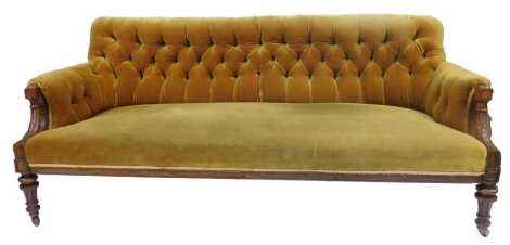 A 19thC walnut framed sofa, upholstered in gold coloured draylon fabric with a buttoned back, carved arms with leaf decoration, on turned and fluted legs, on brass castors, 195cm wide.