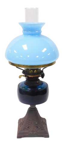 A late 19thC Duplex oil lamp, with a blue glass reservoir and cast iron foliate embossed base, with chimney and turquoise glass shade, 51.5cm high.