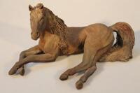 A cast metal sculpture of a recumbent horse