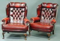 A pair of red leather Chesterfield style wingback armchairs.