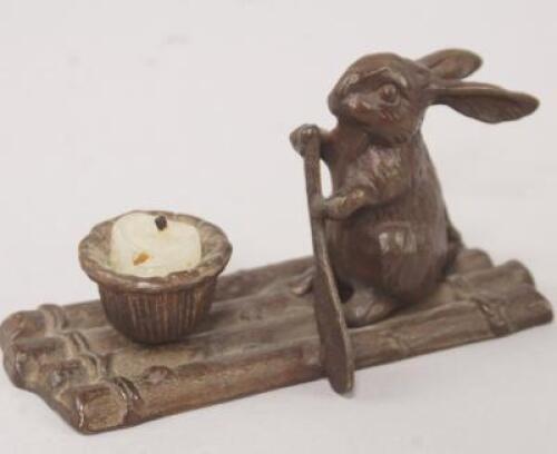 A small bronze candle holder in the form of a hare on a wooden raft