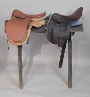 Two brown leather saddles and a painted pine saddle stand.