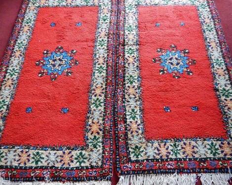 A pair of rugs with blue flowerhead medallions on a red ground