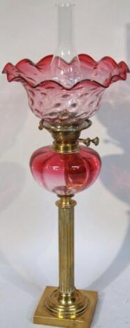 An Edwardian cranberry glass and brass oil lamp