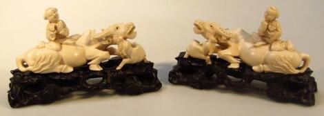 A pair of Chinese figures of children riding water buffalo on carved hardwood bases