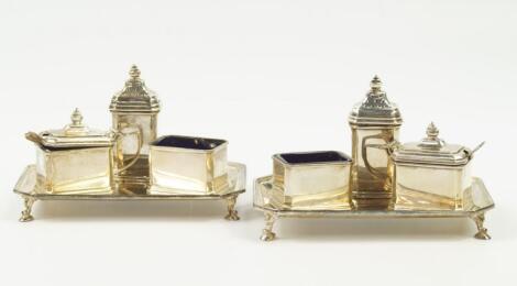 A near pair of George V silver condiment sets on trays