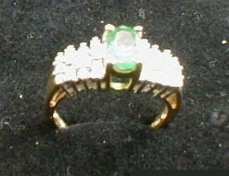 A ladies ring set with a central oval emerald 7mm x 5mm flanked by alternating