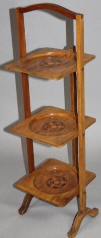 An early 20thC beech and marquetry inlaid three tier cake stand