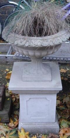 A stone semi fluted garden urn on a square plinth