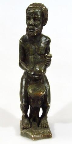 An African tribal carved stone figure of a gentleman standing before drum