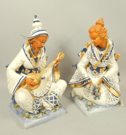 A pair of Italian 20thC pottery figures modelled as a seated geisha girl and male musician