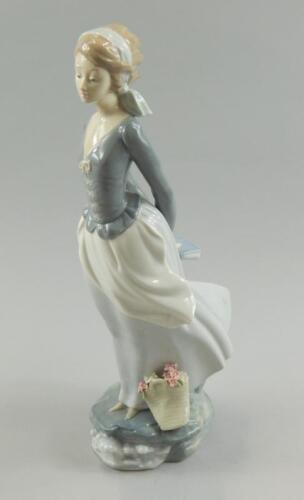 A Lladro porcelain figure of a lady with a basket of flowers carrying a book