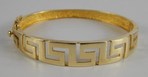 A yellow metal bangle in an open work Greek Key design