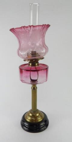 A Victorian brass oil lamp with a cranberry glass reservoir