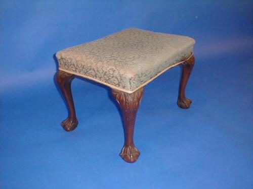 An upholstered foot stool on cabriole legs with ball and claw feet and carved knees