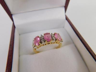 A three stone pink sapphire ring interspersed by pairs of diamonds at intervals