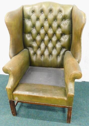 A green leather upholstered wingback chair in George III style