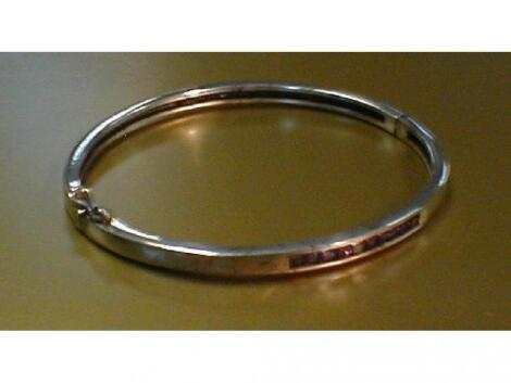 A narrow white metal hinged bangle with channel set lilac stones to the front