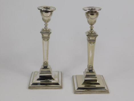 A pair of Edwardian Adam style candlesticks of urn and plinth form