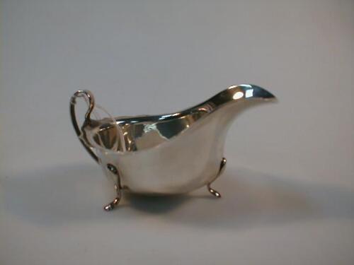 A silver sauce boat, with a bracketed rim and strap handle, on three pad