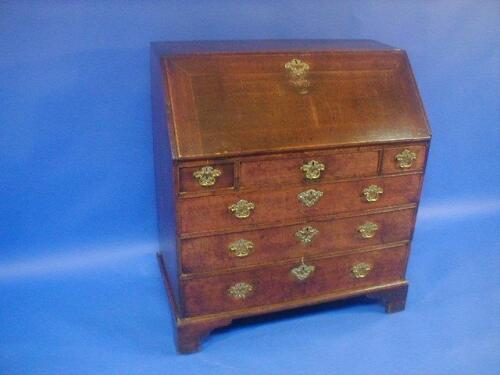 A George III oak bureau with fall flap revealing a fitted interior over