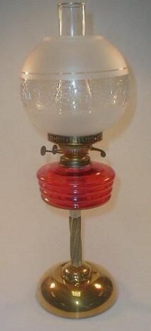 A brass oil lamp, with a cranberry glass reservoir supported on an embossed