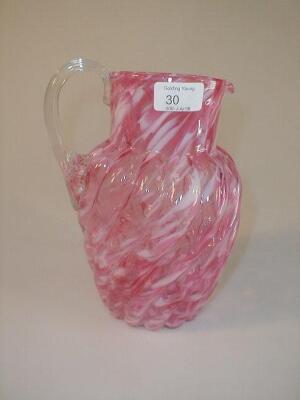 A cranberry glass water jug of wrythen form with a clear glass reeded loop handle