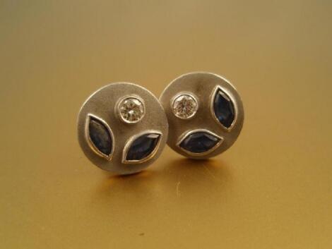 A pair of round stud earrings on posts set with two marquise cut sapphires