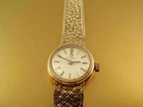 A ladies 9ct Omega round faced wrist watch on a 9ct gold integral bracelet