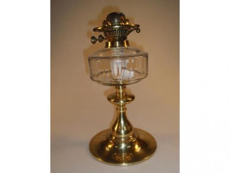 An early 20thC double burner oil lamp with clear glass reservoir on a brass column