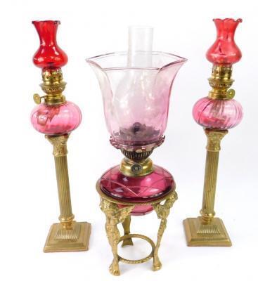 A pair of brass Corinthian column and cranberry glass oil lamps