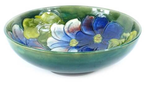 A Moorcroft Clematis pattern bowl, decorated with flowers, on a green ground, impressed mark and initials to underside, also with paper label, 26cm diameter.