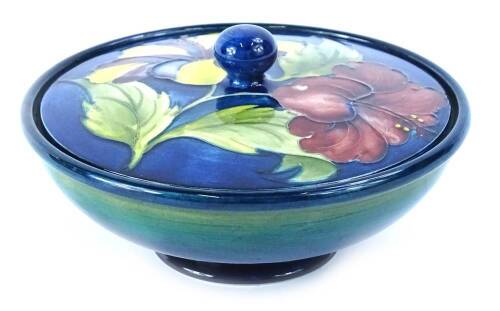 A Walter Moorcroft Hibiscus pattern bowl and cover, decorated with flowers, on a cobalt blue and turquoise ground, impressed mark and printed label to underside, 16cm diameter.