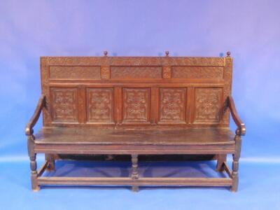 A 17thC oak settle, the panel back with tracery carving and vine and foliate