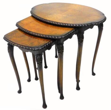 A nest of three walnut tables, each with an oval quarter veneered top, with a carved border on cabriole legs, the largest 60cm W.