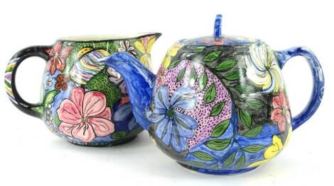 Two similar Art Deco style teapots, each decorated with an all over design of flowers on a blue black and orange ground, initials MAW.