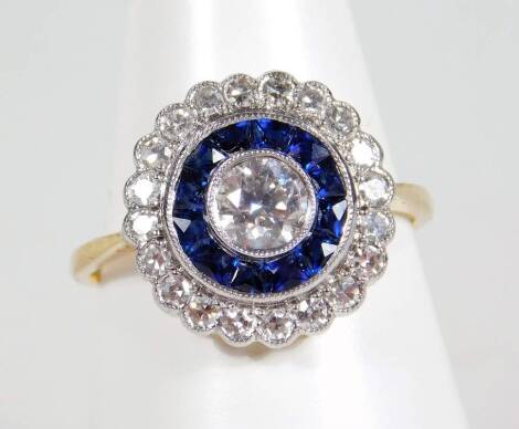 An Art Deco sapphire and diamond dress ring, of circular design with layers of diamonds and sapphires, the centre set with a round brilliant cut diamond, in rub over setting approx 0.35cts, surrounded by square cut sapphires, further bordered by tiny diam