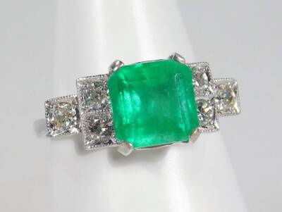 A white gold emerald and diamond ring, the claw set central stone flanked by three diamonds to each shoulder, each diamond approx 0.10cts, with plain shank, believed to be 18ct gold, 4g all in.