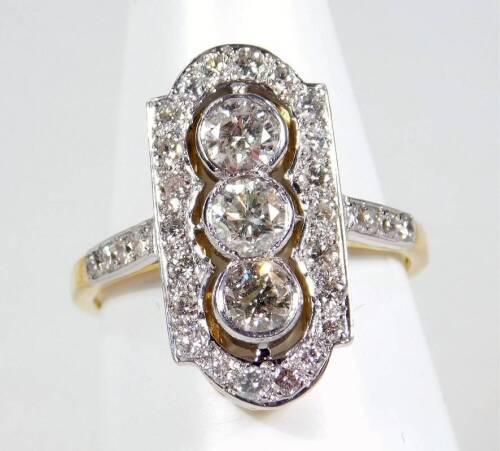 An Art Deco diamond dress ring, the ring head of rectangular shaped form, set with three round brilliant cut diamonds, in rub over setting, each approx 0.20cts each, surrounded by a border of round brilliant cut tiny diamonds, in pave setting, with diamon