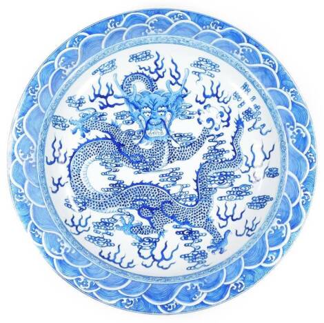 A Chinese blue and white porcelain charger, decorated with dragon with an outer geometric banding, with a partial design verso, on a circular foot, Kangxi style double line flowerhead mark verso, but later, 49cm Dia.